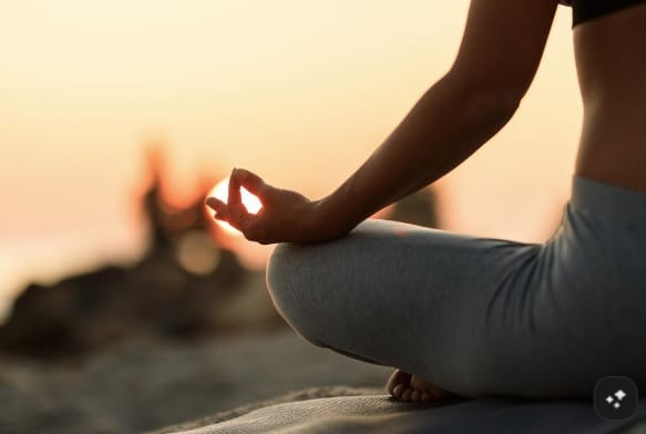 Persona meditando sentada junto al mar al atardecer