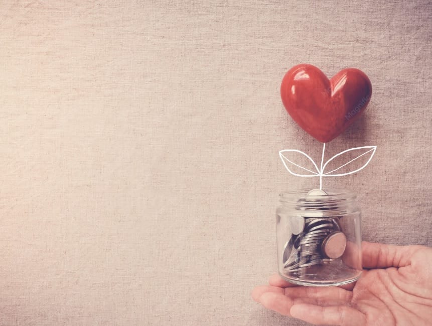 Mano sosteniendo un bote de cristal con monedas del que brota un corazón rojo